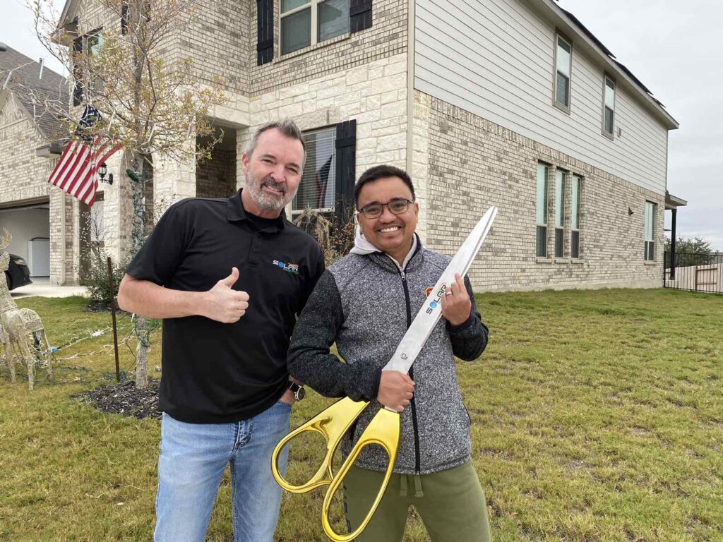 Energy Consultant next to Homeowner that went solar holding a pair of large scissors